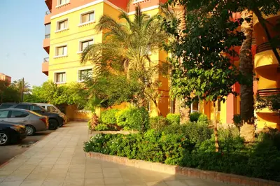 a yellow building with cars parked in a parking lot at Esplanada Beach Apartment, no single men in Hurghada