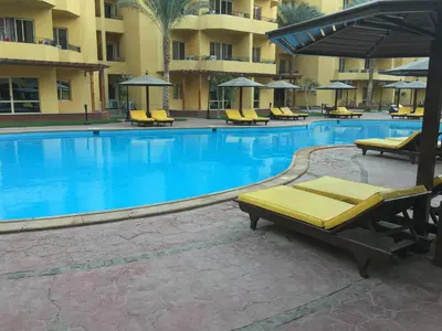 a large swimming pool with yellow chairs and umbrellas at Pool View Apartments at British Resort - Unit 13 in Hurghada