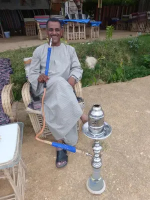 a man is sitting in a chair with a stick in his mouth at Terrasses et Jardins sur le Nil chez Hagag rive Ouest in Luxor