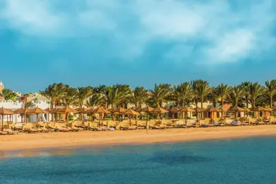 a beach with chairs and palm trees and houses at Sunrise Royal Makadi Resort in Hurghada
