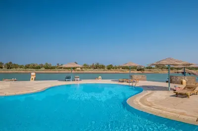 a large blue swimming pool with chairs and umbrellas at El Gouna 1 Bedroom Apartment west golf ground floor in Hurghada