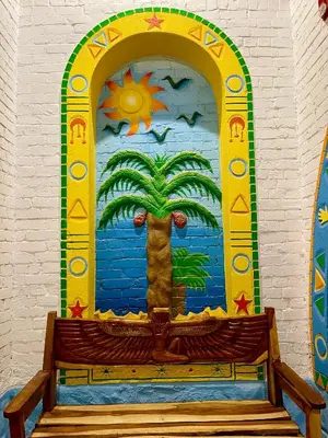 a bench in front of a mural of a palm tree at Kato Dool Wellness Resort in Aswan
