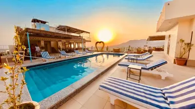 a pool at a hotel with chairs and the sunset at Thebes Hotel in Luxor