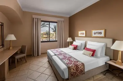 a bedroom with a bed and a desk and a window at JAZ Makadi Saraya Resort in Hurghada
