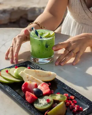 a woman holding a green drink next to a plate of fruit at Siva Grand Beach in Hurghada