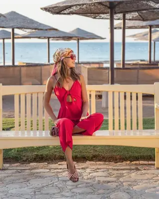 a woman in a red dress sitting on a bench at the beach at Makadi Palace - Couples and Families Only in Hurghada
