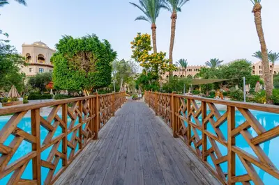 a wooden bridge over a pool at a resort with palm trees at Makadi Palace - Couples and Families Only in Hurghada