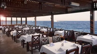a restaurant with white tables and chairs and the ocean at Arabella Azur Resort in Hurghada