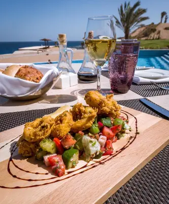 a plate of food on a table with a glass of wine at The Oberoi Beach Resort, Sahl Hasheesh in Hurghada