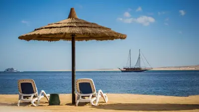 two chairs and an umbrella on a beach with a boat at Sky View Suites Hotel in Hurghada