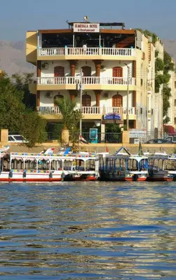 a large building with boats docked in the water at El Mesala Hotel in Luxor