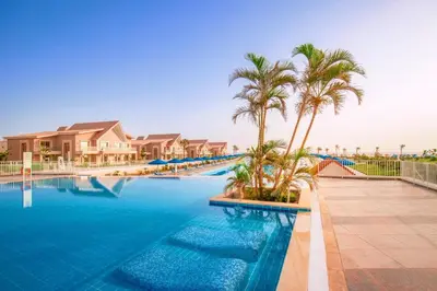 a swimming pool with palm trees and houses at Pickalbatros Sea World Resort - Marsa Alam- 
