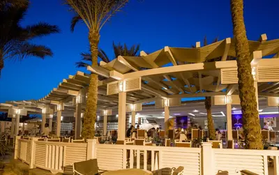 a restaurant with chairs and palm trees at night at Mirage Bay Resort & Aqua Park in Hurghada