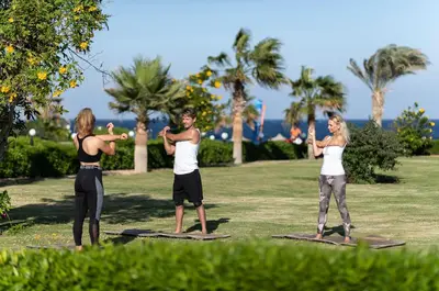 a group of people standing on yoga mats in a park at Three Corners Happy Life Beach Resort in Abu Dabab