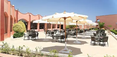 an outdoor patio with tables and chairs and umbrellas at Three Corners Happy Life Beach Resort in Abu Dabab