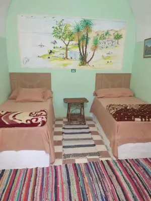 a room with two beds and a table in it at Aswan Nubian House in Aswan