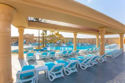 a pool with blue lounge chairs on a patio at Stella Gardens Resort & Spa, Makadi Bay in Hurghada