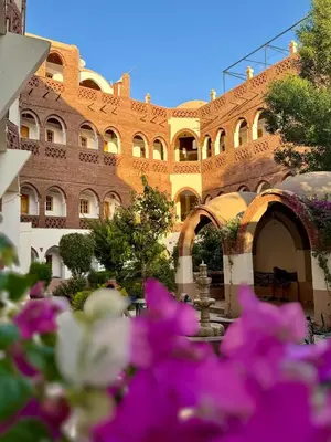 a large brick building with purple flowers in front of it at Hotel Sheherazade Luxor in Luxor