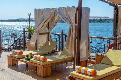 a deck with two chairs and a table on the water at Sonesta Dahabeya Amirat I - Nile Cruise Ship From Luxor to Aswan 7 nights in Luxor