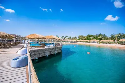 a dock with boats and umbrellas on a beach at Sunrise Aqua Joy Resort in Hurghada