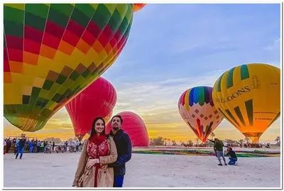 a man and woman standing in front of a group of hot air balloons at Golden Palace Garden in Luxor