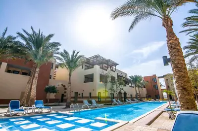 a pool with palm trees and chairs and a building at Marina Residence Suites Port Ghalib in Port Ghalib