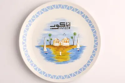 a plate with a house on the water with sailboats at Anakob in Aswan