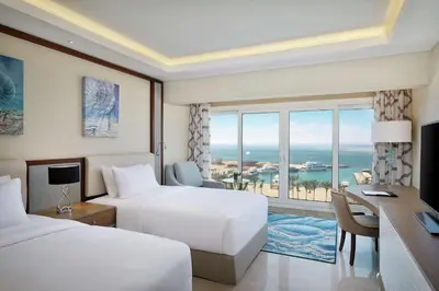 a hotel room with two beds and a desk and a window at Hilton Hurghada Plaza Hotel in Hurghada