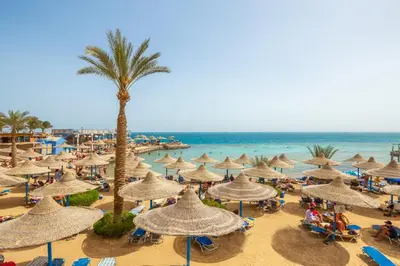 a beach with a lot of umbrellas and the ocean at King Tut Aqua Park Beach Resort in Hurghada