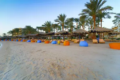 a beach with many chairs and umbrellas and palm trees at Regina Resort and Aqua Park Hurghada in Hurghada
