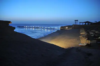 a beach with a pier and the ocean at night at JAZ Neo Reef Marsa in Coraya Bay