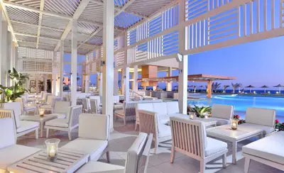 a restaurant with white chairs and tables and a pool at JAZ Elite Maraya in Coraya Bay