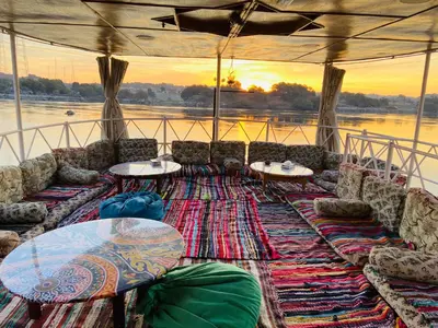a boat with tables and couches on the water at Kendaka Nubian House in Aswan