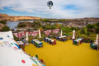 a restaurant with tables and umbrellas and a river at Onaty Ka Guest House in Aswan