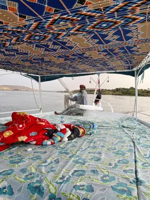 a person laying on a boat under a canopy at Felucca Sailing Boat Overnight Experience in Aswan