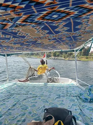 a man sitting on a boat in the water at Felucca Sailing Boat Overnight Experience in Aswan