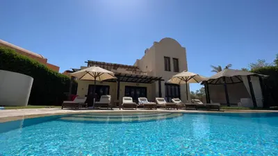 a pool with chairs and umbrellas next to a house at Villa - Sleeps 6 - Heated Pool - Garden - Parking in Hurghada