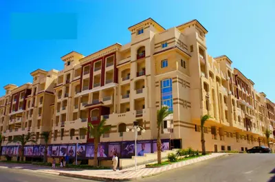 a large yellow building with palm trees in front of it at Studio H in Florenza Khamsin in Hurghada