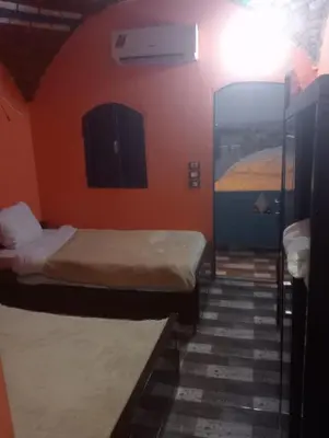 a room with two beds in a room with orange walls at NeNeKaTo Nubian House in Aswan