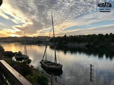 two boats are docked on a river at sunset at NOBATiA Guest House in Aswan