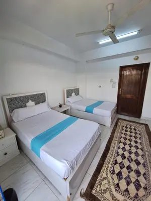 two beds in a white bedroom with a rug at NOBATiA Guest House in Aswan