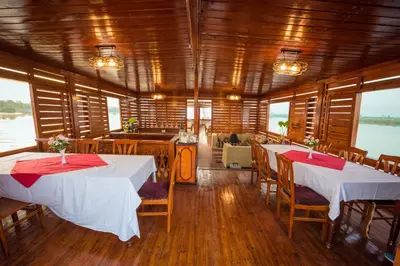 a dining room with two tables and chairs and windows at Dahabiya ECO Queen Cleopatra in Esna
