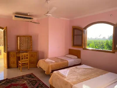 a room with two beds and a window and a table at Elsanosy Family Guest House - Luxor in Luxor