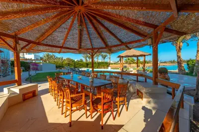 an outdoor dining area with a table and chairs under a large umbrella at 4 Bedroom Villa with Heated Pool, Jacuzzi & Lagoon View in Phase 4 in Hurghada