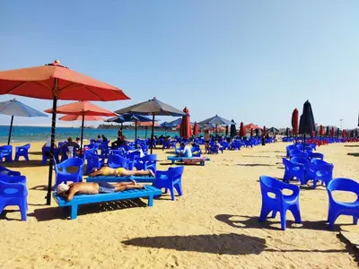 a beach with blue chairs and umbrellas and people laying on them at apartment with separate entrance near Arabia hotel in Hurghada