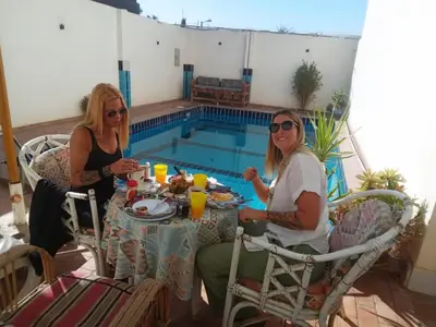 two women sitting at a table next to a swimming pool at Sinderella Private Pool Villa in Luxor