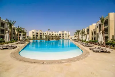 a large swimming pool with chairs and umbrellas at Ollystays Mangroovy 2 BR Beach and Pool Free access in Hurghada