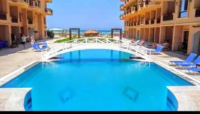 a bridge over a swimming pool with chairs and the ocean at Turtles Beach Resort - Sea View in Hurghada