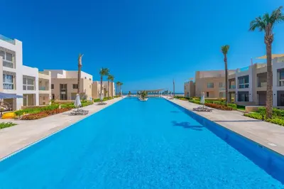 a large swimming pool with palm trees and buildings at Mangroovy 3BR Apartment Private Beach & Pool View in Hurghada