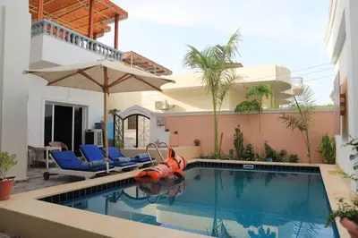 a swimming pool with chairs and an umbrella next to a house at Nefertarie Guest House in Luxor